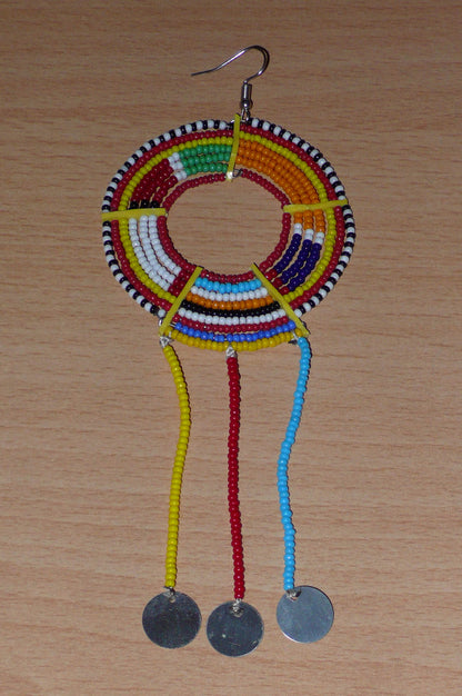 Longue mono boucle d'oreille africaine Massai à porter sur une seule oreille pour un effet visuel asymétrique. Elle se compose de perles de rocaille multicolores enfilées sur des fils de fer montés en cercles fixés sur des charnières en plastique recyclé jaune, et se prolonge de franges perlées ornées de disques en métal. Surdimensionnée, cette mono boucle d'oreille mesure 15.5 cm de long et se porte sur une oreille percée.