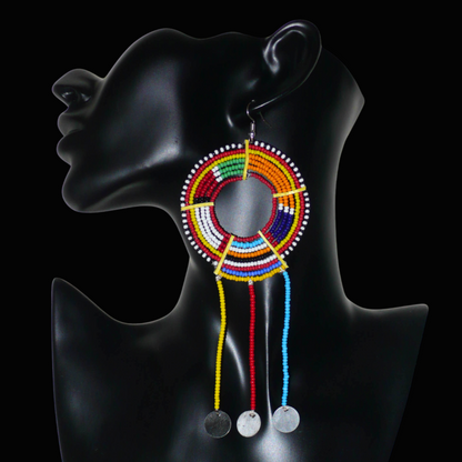 Longue mono boucle d'oreille africaine Massai à porter sur une seule oreille pour un effet visuel asymétrique. Elle se compose de perles de rocaille multicolores enfilées sur des fils de fer montés en cercles fixés sur des charnières en plastique recyclé jaune, et se prolonge de franges perlées ornées de disques en métal. Surdimensionnée, cette mono boucle d'oreille mesure 15.5 cm de long et se porte sur une oreille percée.