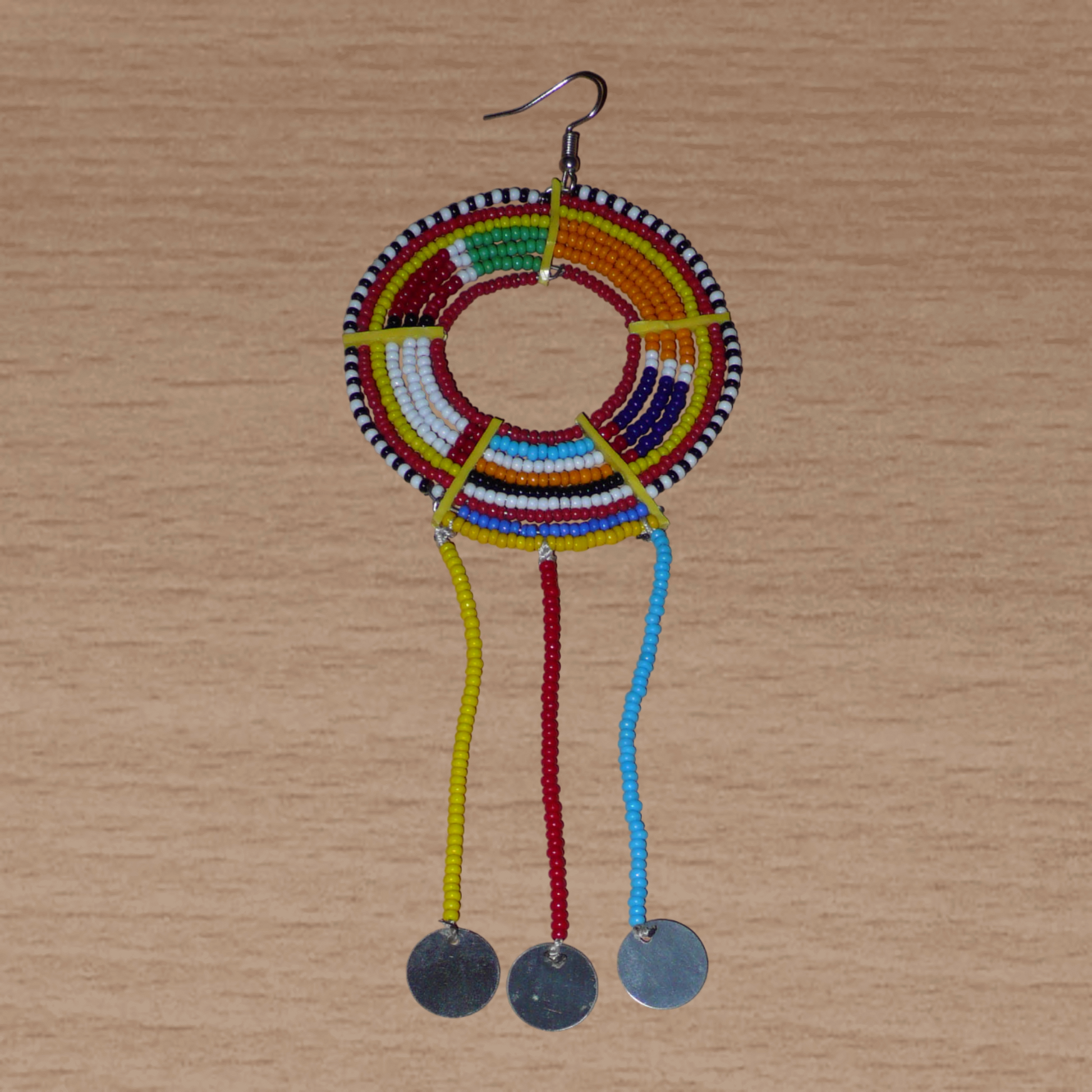 Longue mono boucle d'oreille africaine Massai à porter sur une seule oreille pour un effet visuel asymétrique. Elle se compose de perles de rocaille multicolores enfilées sur des fils de fer montés en cercles fixés sur des charnières en plastique recyclé jaune, et se prolonge de franges perlées ornées de disques en métal. Surdimensionnée, cette mono boucle d'oreille mesure 15.5 cm de long et se porte sur une oreille percée.