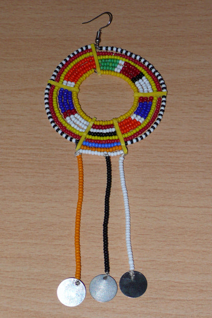 Mono boucle d'oreille confectionnée dans la plus pure tradition tribale Massai, à porter sur une seule oreille pour un effet visuel asymétrique, composée de perles de rocaille jaunes et multicolores enfilées sur des fils de fer montés en cercles et se prolonge de franges perlées ornées de disques métalliques. Surdimensionnée, elle mesure 16 cm de long et se porte sur des oreilles percées.