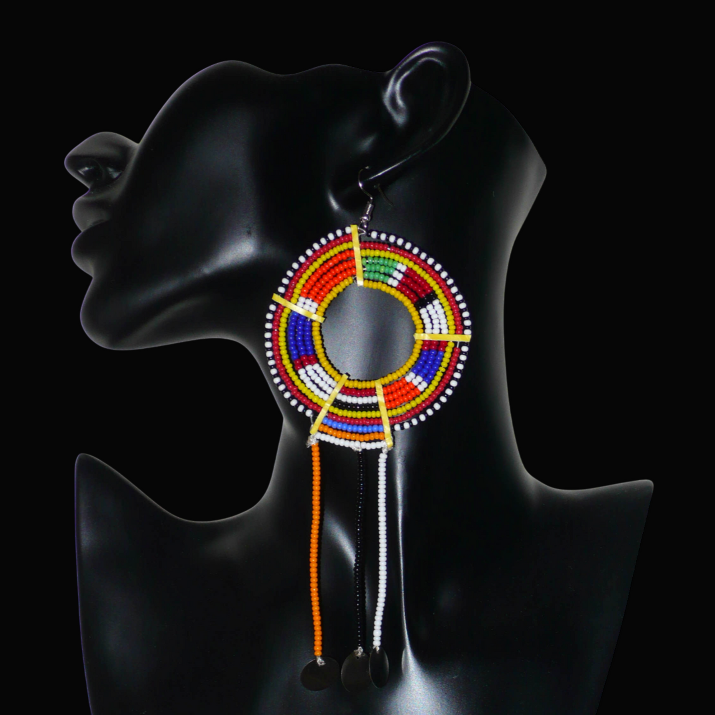 Mono boucle d'oreille confectionnée dans la plus pure tradition tribale Massai, à porter sur une seule oreille pour un effet visuel asymétrique, composée de perles de rocaille jaunes et multicolores enfilées sur des fils de fer montés en cercles et se prolonge de franges perlées ornées de disques métalliques. Surdimensionnée, elle mesure 16 cm de long et se porte sur des oreilles percées.