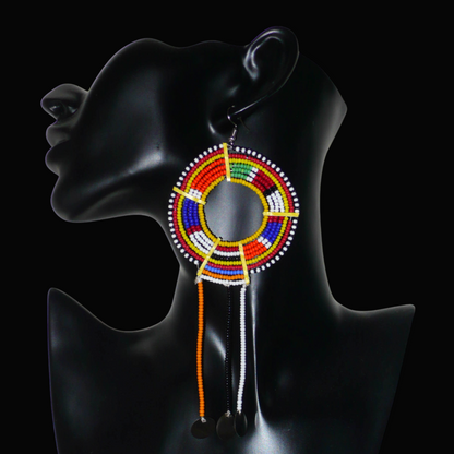 Mono boucle d'oreille confectionnée dans la plus pure tradition tribale Massai, à porter sur une seule oreille pour un effet visuel asymétrique, composée de perles de rocaille jaunes et multicolores enfilées sur des fils de fer montés en cercles et se prolonge de franges perlées ornées de disques métalliques. Surdimensionnée, elle mesure 16 cm de long et se porte sur des oreilles percées.