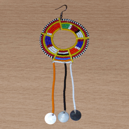 Mono boucle d'oreille confectionnée dans la plus pure tradition tribale Massai, à porter sur une seule oreille pour un effet visuel asymétrique, composée de perles de rocaille jaunes et multicolores enfilées sur des fils de fer montés en cercles et se prolonge de franges perlées ornées de disques métalliques. Surdimensionnée, elle mesure 16 cm de long et se porte sur des oreilles percées.
