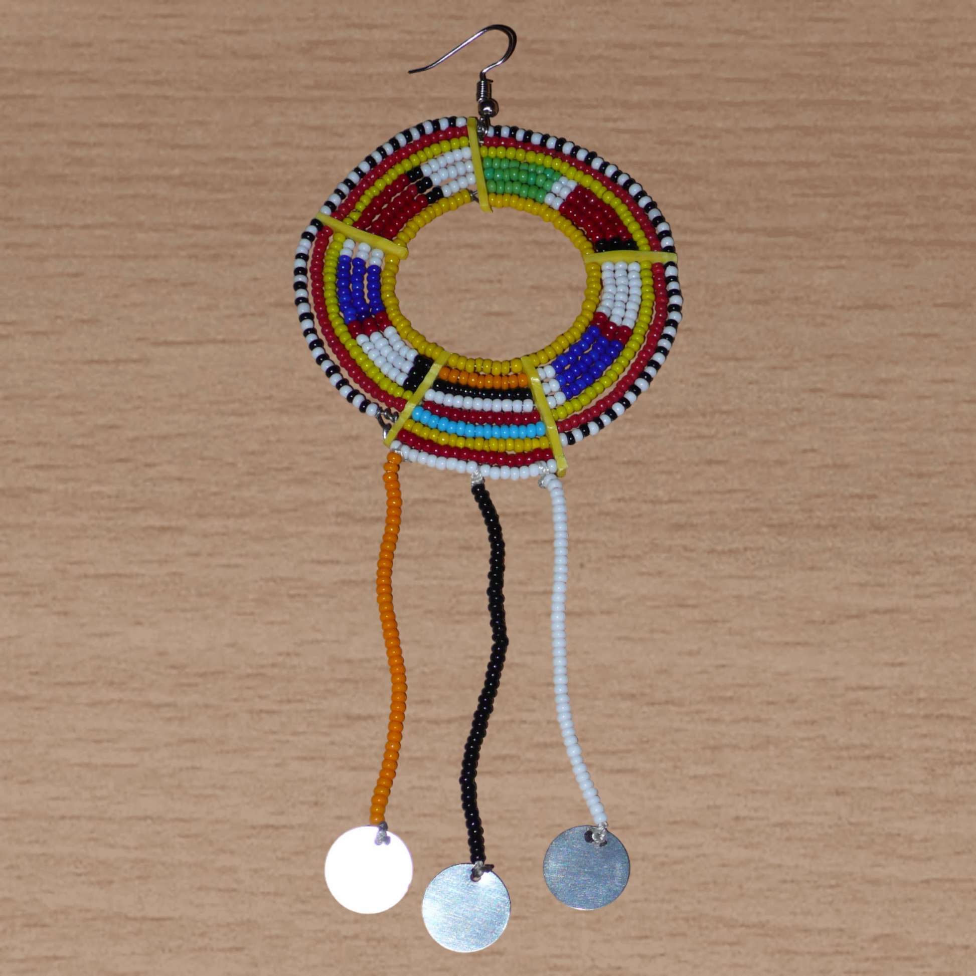 Mono boucle d'oreille à porter sur une seule oreille pour un effet visuel asymétrique : elle se compose de perles de rocaille jaunes et multicolores enfilées sur des fils de fer montés en cercles fixés sur des charnières en plastique recyclé jaune, et se prolonge de franges perlées ornées de disques métalliques. Surdimensionnée, elle mesure 16 cm de long.