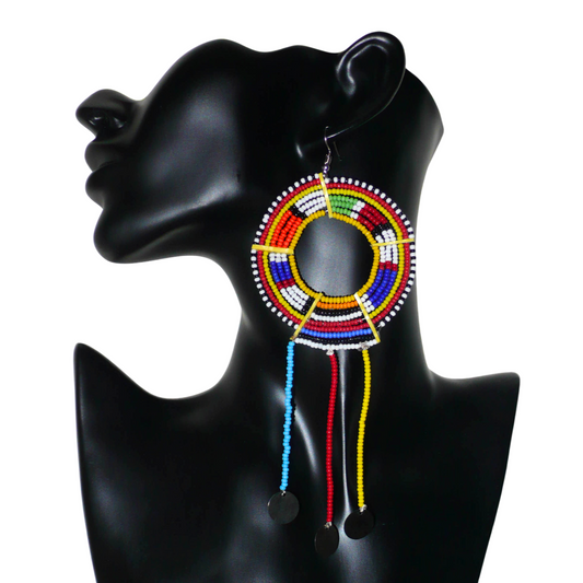 Mono boucle d'oreille à franges fabriquée au Kenya dans la tradition ethnique Massai. À porter sur une seule oreille pour un effet visuel asymétrique, ce bijou se compose de perles de rocaille multicolores glissées sur des fils de fer montés en cercles fixés sur des charnières en plastique recyclé jaune ; il se prolonge de franges perlées ornées de disques en métal. Surdimensionnée, elle mesure 16.5 cm de long et 6.5 cm de large, et se porte sur une oreille percée.