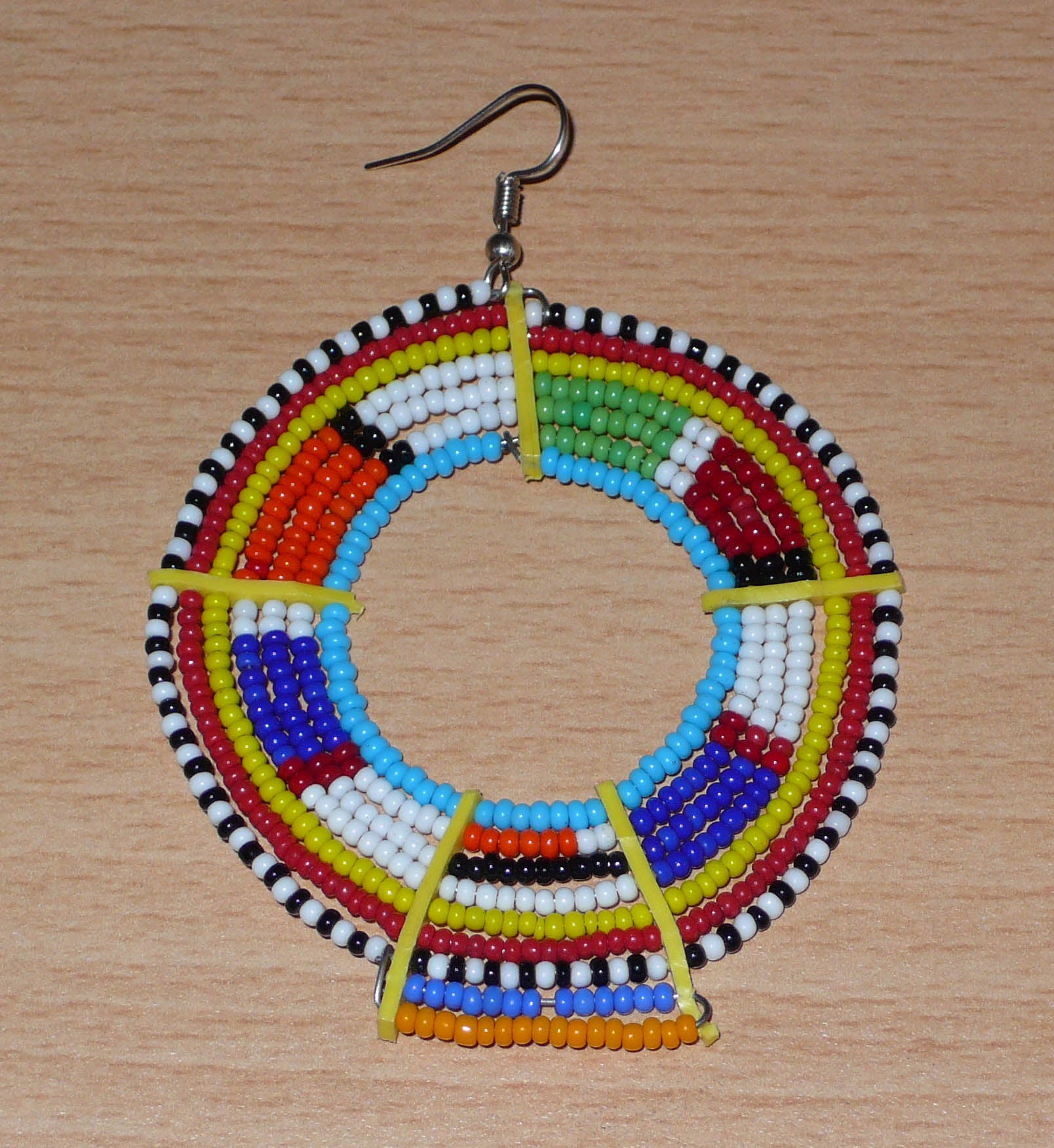 Ajoutez une touche ultra colorée à votre look avec cette mono boucle africaine Massai, à porter sur une seule oreille pour un effet visuel asymétrique ! De fabrication traditionnelle kenyane, ce bijou artisanal se compose de perles de rocaille bleues et multicolores glissées sur des fils de fer montés en cercles et fixés sur des charnières en plastique recyclé jaune. Surdimensionnée, elle mesure 8.5 cm de long et 6 cm de large, et se porte avec un crochet sur une oreille percée.