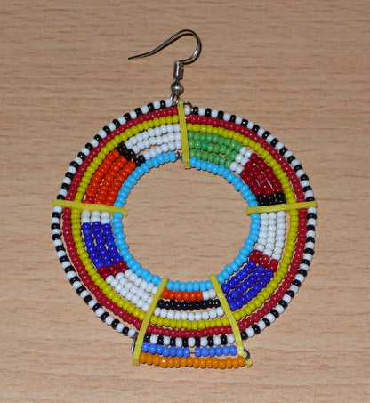 Ajoutez une touche ultra colorée à votre look avec cette mono boucle africaine Massai, à porter sur une seule oreille pour un effet visuel asymétrique ! De fabrication traditionnelle kenyane, ce bijou artisanal se compose de perles de rocaille bleues et multicolores glissées sur des fils de fer montés en cercles et fixés sur des charnières en plastique recyclé jaune. Surdimensionnée, elle mesure 8.5 cm de long et 6 cm de large, et se porte avec un crochet sur une oreille percée.
