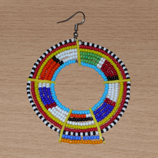 Ajoutez une touche ultra colorée à votre look avec cette mono boucle africaine Massai, à porter sur une seule oreille pour un effet visuel asymétrique ! De fabrication traditionnelle kenyane, ce bijou artisanal se compose de perles de rocaille bleues et multicolores glissées sur des fils de fer montés en cercles et fixés sur des charnières en plastique recyclé jaune. Surdimensionnée, elle mesure 8.5 cm de long et 6 cm de large, et se porte avec un crochet sur une oreille percée.