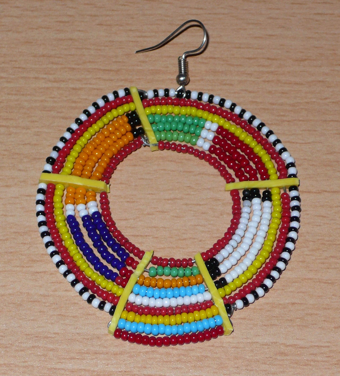 Affirmez votre style afro et apportez de la couleur à votre look avec cette mono boucle africaine de tradition Massai, à porter sur une seule oreille pour un effet visuel asymétrique !  De fabrication artisanale kenyane, ce bijou unique se compose de perles de rocaille rouges et multicolores enfilées sur des fils de fer montés en cercles et fixés sur des charnières en plastique recyclé jaune. Surdimensionnée, cette mono boucle mesure 8 cm de long et se porte sur une oreille percée.