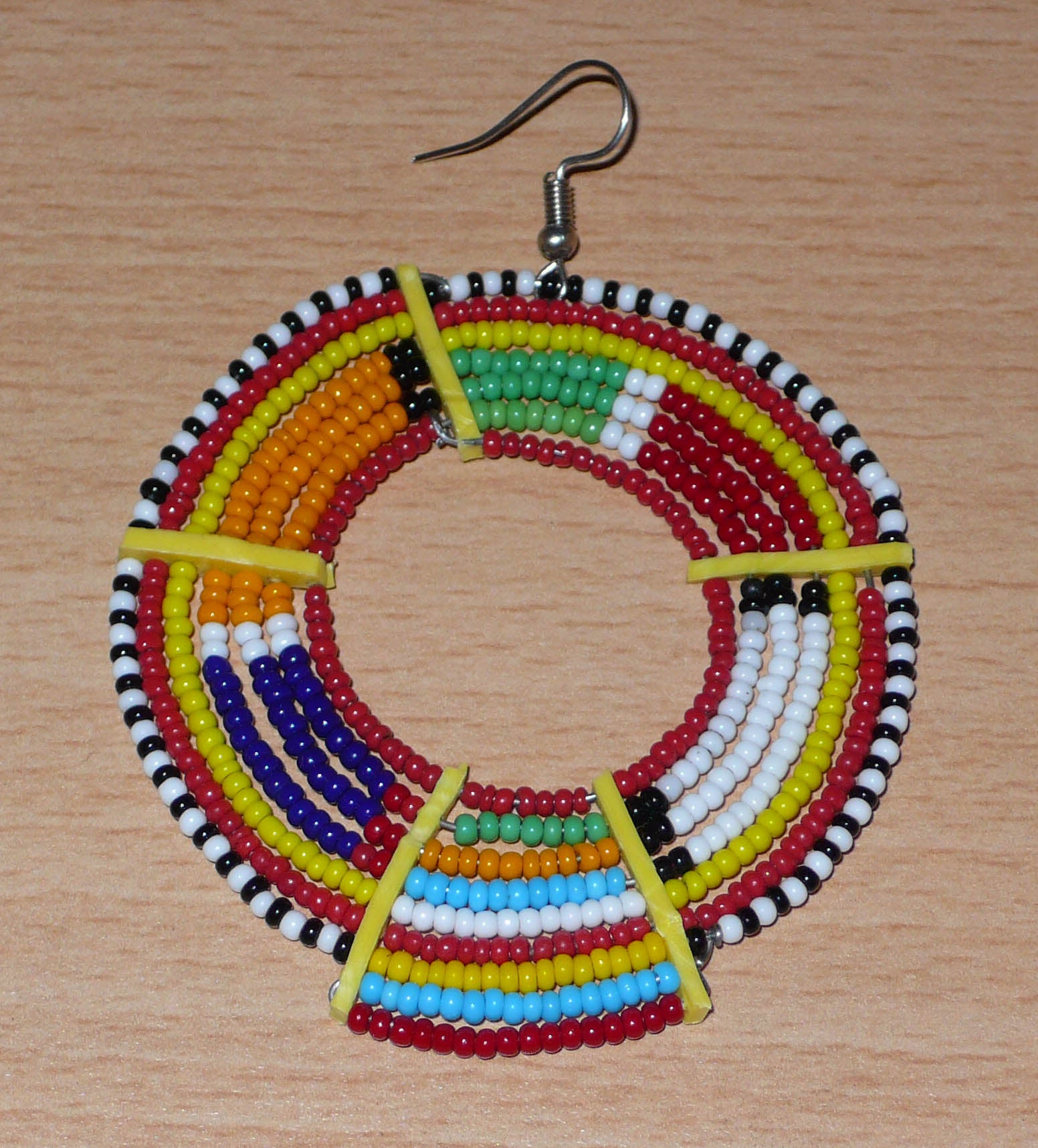 Affirmez votre style afro et apportez de la couleur à votre look avec cette mono boucle africaine de tradition Massai, à porter sur une seule oreille pour un effet visuel asymétrique !  De fabrication artisanale kenyane, ce bijou unique se compose de perles de rocaille rouges et multicolores enfilées sur des fils de fer montés en cercles et fixés sur des charnières en plastique recyclé jaune. Surdimensionnée, cette mono boucle mesure 8 cm de long et se porte sur une oreille percée.