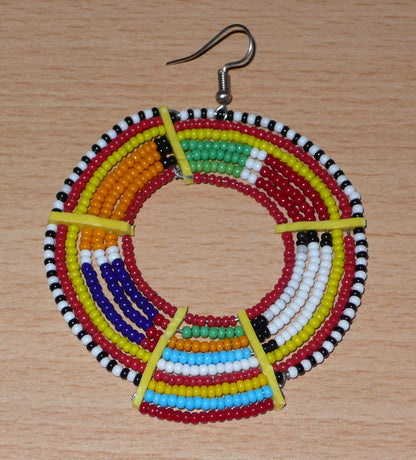 Affirmez votre style afro et apportez de la couleur à votre look avec cette mono boucle africaine de tradition Massai, à porter sur une seule oreille pour un effet visuel asymétrique !  De fabrication artisanale kenyane, ce bijou unique se compose de perles de rocaille rouges et multicolores enfilées sur des fils de fer montés en cercles et fixés sur des charnières en plastique recyclé jaune. Surdimensionnée, cette mono boucle mesure 8 cm de long et se porte sur une oreille percée.