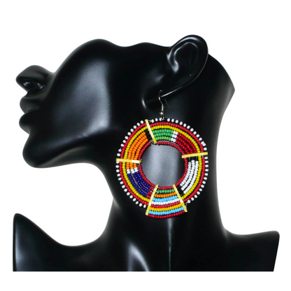 Affirmez votre style afro et apportez de la couleur à votre look avec cette mono boucle africaine de tradition Massai, à porter sur une seule oreille pour un effet visuel asymétrique !  De fabrication artisanale kenyane, ce bijou unique se compose de perles de rocaille rouges et multicolores enfilées sur des fils de fer montés en cercles et fixés sur des charnières en plastique recyclé jaune. Surdimensionnée, cette mono boucle mesure 8 cm de long et se porte sur une oreille percée.