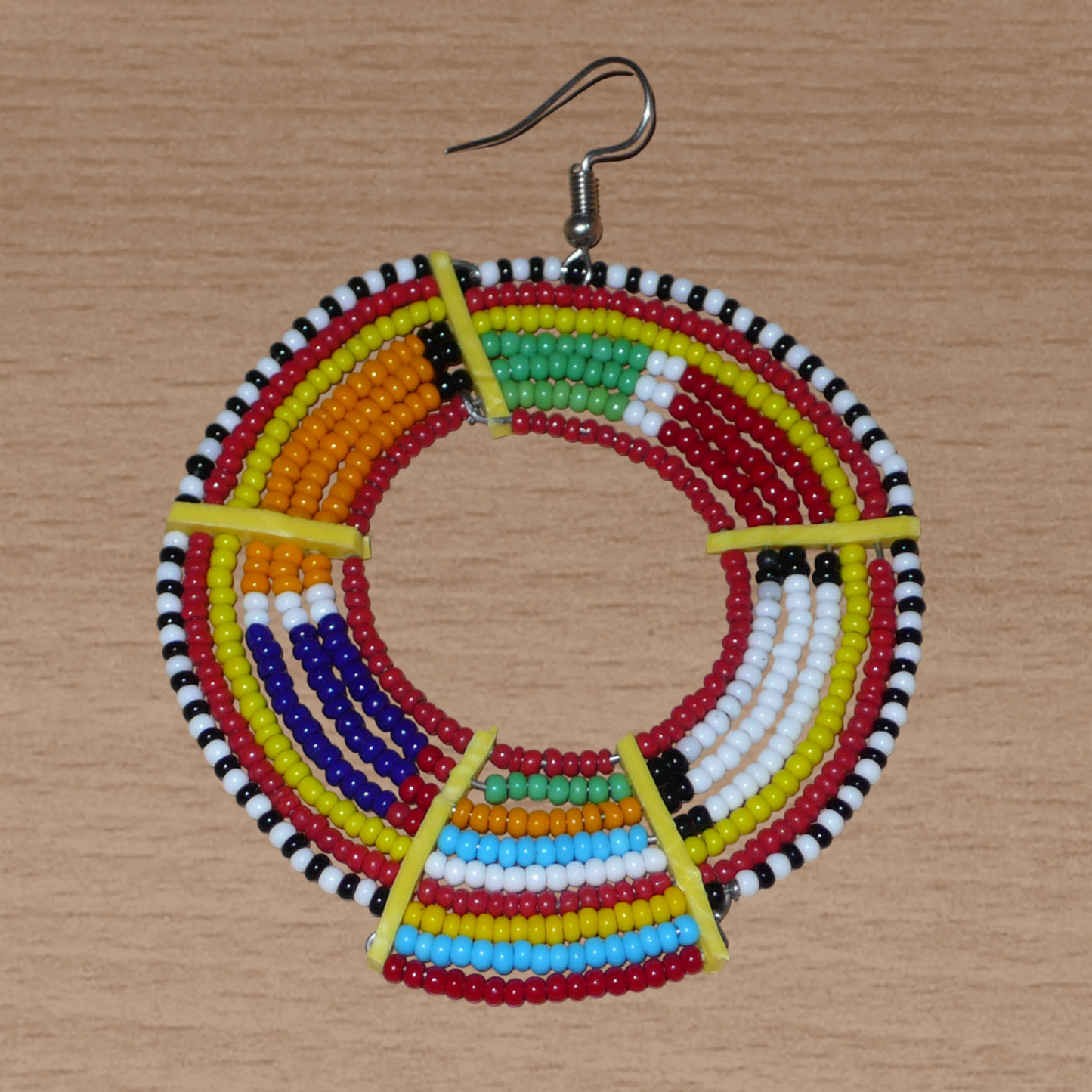 Affirmez votre style afro et apportez de la couleur à votre look avec cette mono boucle africaine de tradition Massai, à porter sur une seule oreille pour un effet visuel asymétrique !  De fabrication artisanale kenyane, ce bijou unique se compose de perles de rocaille rouges et multicolores enfilées sur des fils de fer montés en cercles et fixés sur des charnières en plastique recyclé jaune. Surdimensionnée, cette mono boucle mesure 8 cm de long et se porte sur une oreille percée.