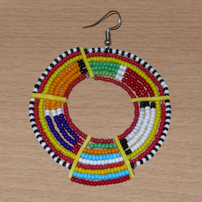 Affirmez votre style afro et apportez de la couleur à votre look avec cette mono boucle africaine de tradition Massai, à porter sur une seule oreille pour un effet visuel asymétrique !  De fabrication artisanale kenyane, ce bijou unique se compose de perles de rocaille rouges et multicolores enfilées sur des fils de fer montés en cercles et fixés sur des charnières en plastique recyclé jaune. Surdimensionnée, cette mono boucle mesure 8 cm de long et se porte sur une oreille percée.
