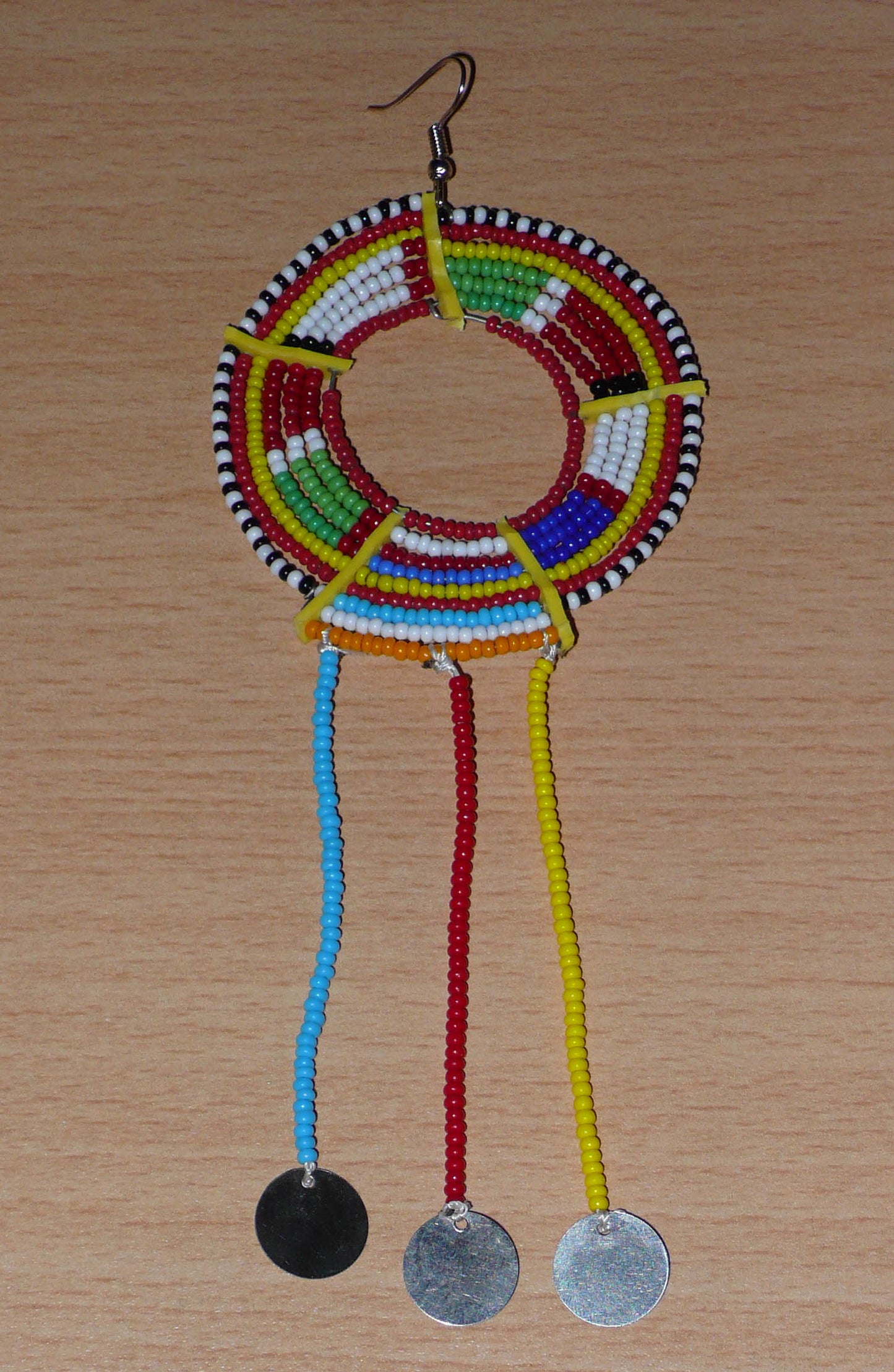 Pièce unique composée de perles de rocaille rouges et multicolores, cette mono boucle d'oreille à franges, confectionnée au Kenya dans la plus pure tradition Massai, est un bijou à porter d'un seul côté, qui apportera à votre look une touche éclatante d'asymétrie visuelle. Surdimensionnée, cette mono boucle au style exotique mesure 16 cm de long et 6 cm de large, et se porte avec un crochet en acier inoxydable sur une oreille percée.