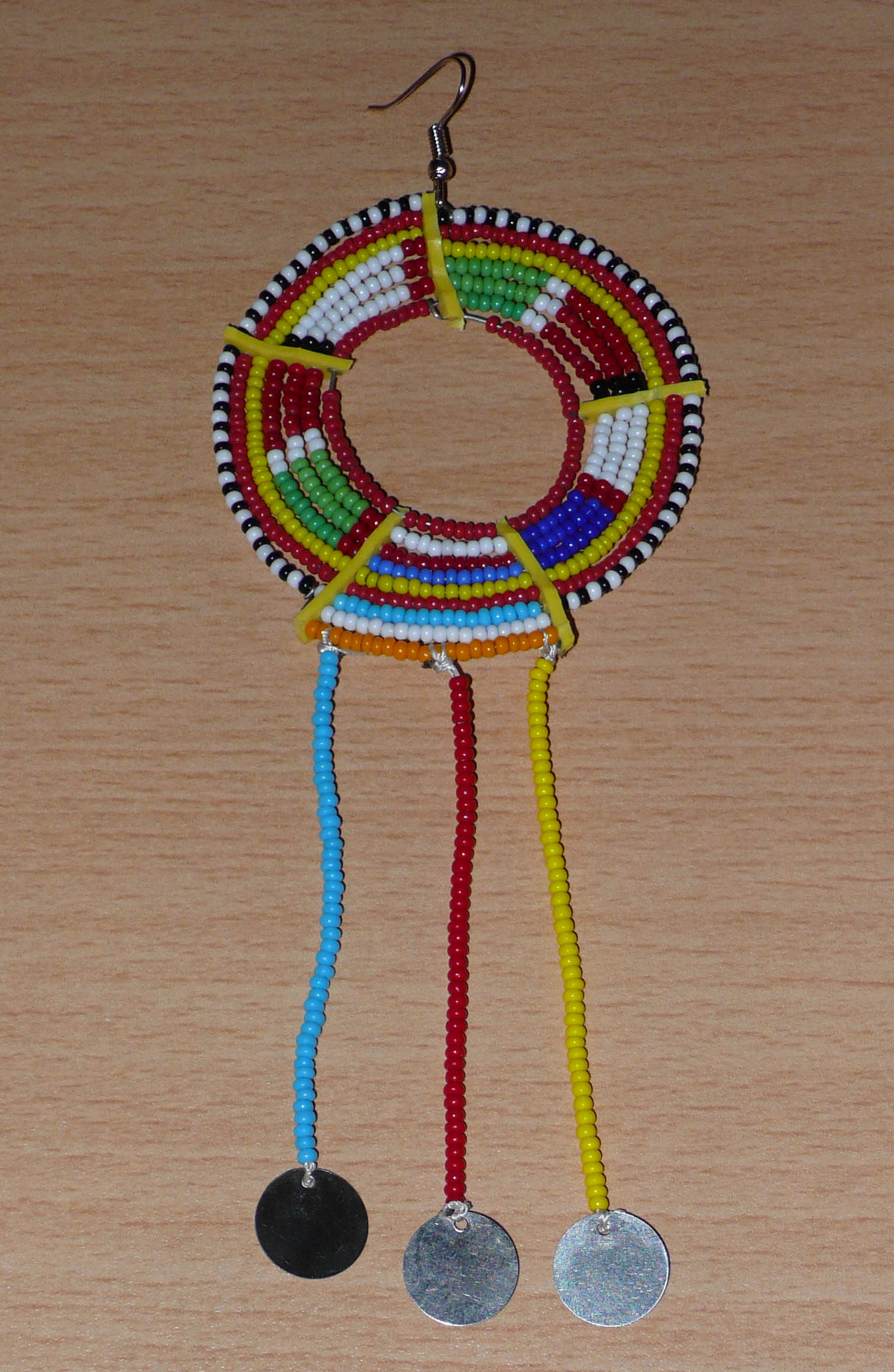 Pièce unique composée de perles de rocaille rouges et multicolores, cette mono boucle d'oreille à franges, confectionnée au Kenya dans la plus pure tradition Massai, est un bijou à porter d'un seul côté, qui apportera à votre look une touche éclatante d'asymétrie visuelle. Surdimensionnée, cette mono boucle au style exotique mesure 16 cm de long et 6 cm de large, et se porte avec un crochet en acier inoxydable sur une oreille percée.