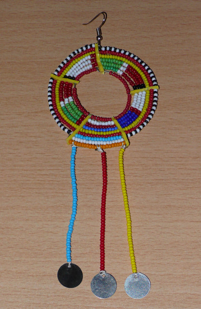 Pièce unique composée de perles de rocaille rouges et multicolores, cette mono boucle d'oreille à franges, confectionnée au Kenya dans la plus pure tradition Massai, est un bijou à porter d'un seul côté, qui apportera à votre look une touche éclatante d'asymétrie visuelle. Surdimensionnée, cette mono boucle au style exotique mesure 16 cm de long et 6 cm de large, et se porte avec un crochet en acier inoxydable sur une oreille percée.