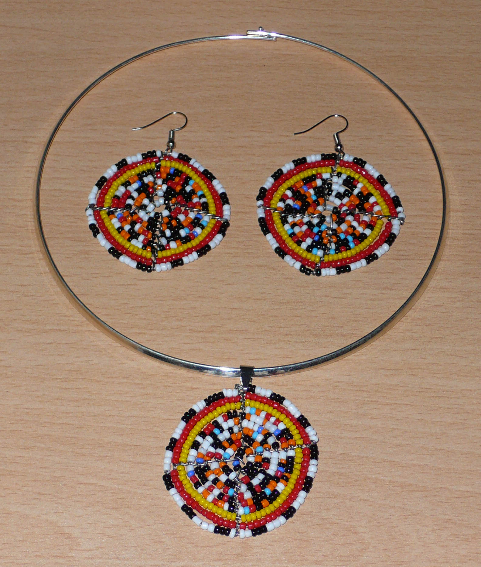 Parure de bijoux au style afro bohème se composant d'un collier ras de cou en laiton orné d'un médaillon fait d'un mélange de perles de rocaille, et d'une paire de boucles d'oreilles assorties.