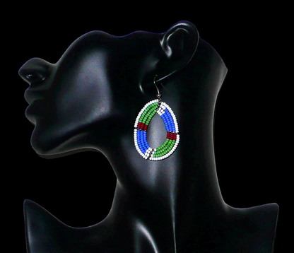 Boucles d'oreilles africaines Massai en forme de gouttes composées de perles de rocaille vertes, bleues, rouges et blanches. Elles mesurent 6 cm de long et 3,5 cm de large et se portent avec des crochets en acier inoxydable sur des oreilles percées.