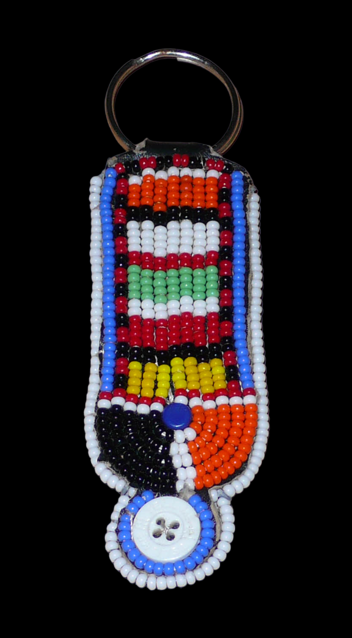 Porte-clés africain à motifs traditionnels Massai composé de perles de rocaille multicolores et de boutons brodés sur un morceau de cuir. Ce porte-clés, brodé sur les deux faces, mesure 10,5 cm de long et 3 cm de large. Il est ici présenté sur un fond noir. Timeless Fineries