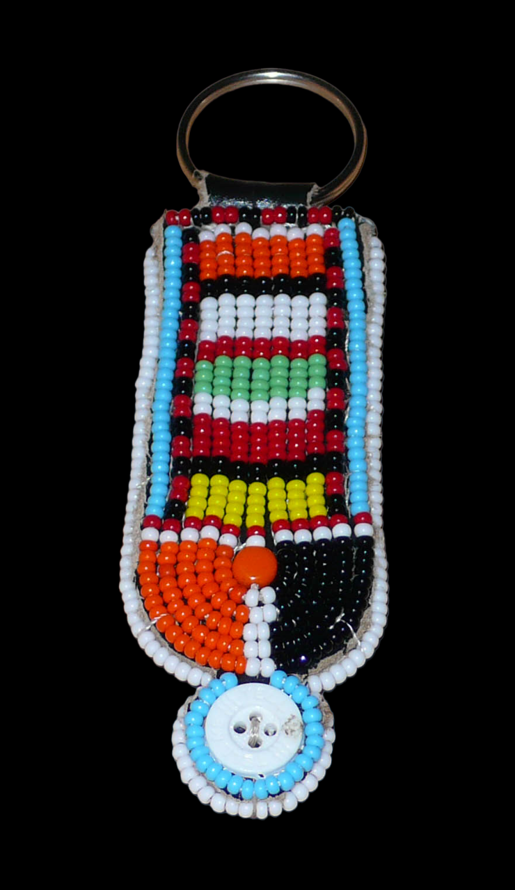 Porte-clés africain à motifs traditionnels Massai composé de perles de rocaille multicolores et de boutons brodés sur un morceau de cuir. Ce porte-clés, brodé sur les deux faces, mesure 10,5 cm de long et 3 cm de large. Timeless Fineries