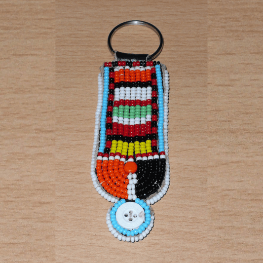 Porte-clés africain à motifs ethniques Massai composé de perles de rocaille multicolores et de boutons brodés sur un morceau de cuir. Ce porte-clés, brodé sur les deux faces, mesure 10,5 cm de long et 3 cm de large.