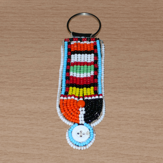 Porte-clés africain à motifs ethniques Massai composé de perles de rocaille multicolores et de boutons brodés sur un morceau de cuir. Ce porte-clés, brodé sur les deux faces, mesure 10,5 cm de long et 3 cm de large.