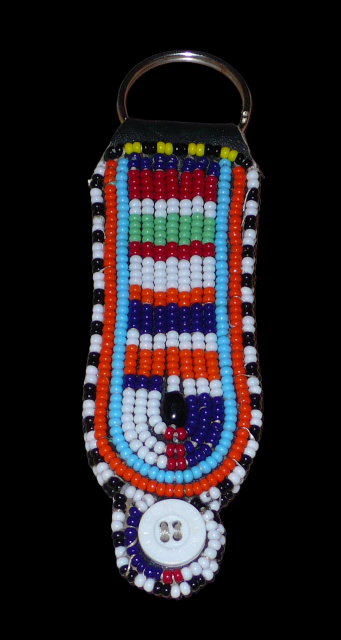 Porte-clés africain à motifs traditionnels Massai composé de perles de rocaille multicolores et de boutons brodés sur un morceau de cuir. Ce porte-clés, brodé sur les deux faces, mesure 10,5 cm de long et 3 cm de large. Photographié sur un fond noir. Timeless Fineries