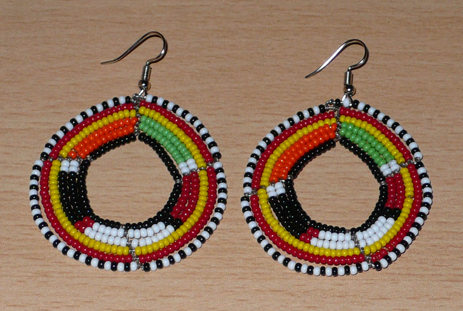 Boucles d'oreilles africaines à motifs ethniques de tradition Massai composées de perles de verre noires et multicolores fixées sur six rangées de fils de fer montés en cercles. De taille moyenne, ces boucles d'oreilles mesurent 7 cm de long et 5 cm de large. Timeless Fineries