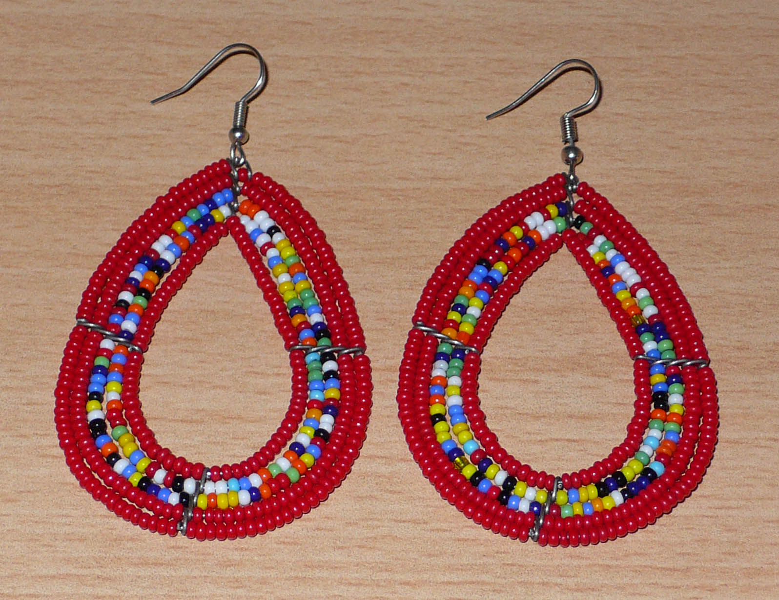 Boucles d'oreilles ethniques multi-rangs en forme de gouttes faites de perles de rocaille rouges et multicolores. Elles mesurent 8 cm de long et 4,5 cm de large, et se portent sur des oreilles percées.