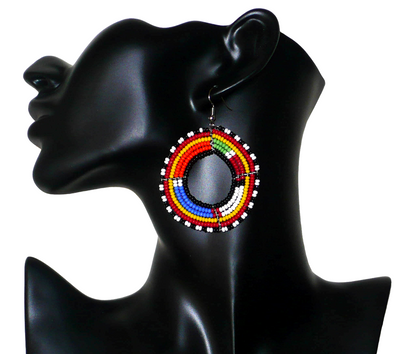 Boucles d'oreilles africaines traditionnelles Massai de 7 cm de long sur 5 cm de large., faites de perles de rocailles multicolores glissées sur 6 rangs de fils de fer montés en forme de cercles. Les couleurs utilisées sont l'orange, le bleu, du blanc, du rouge, du vert, du jaune et du noir.