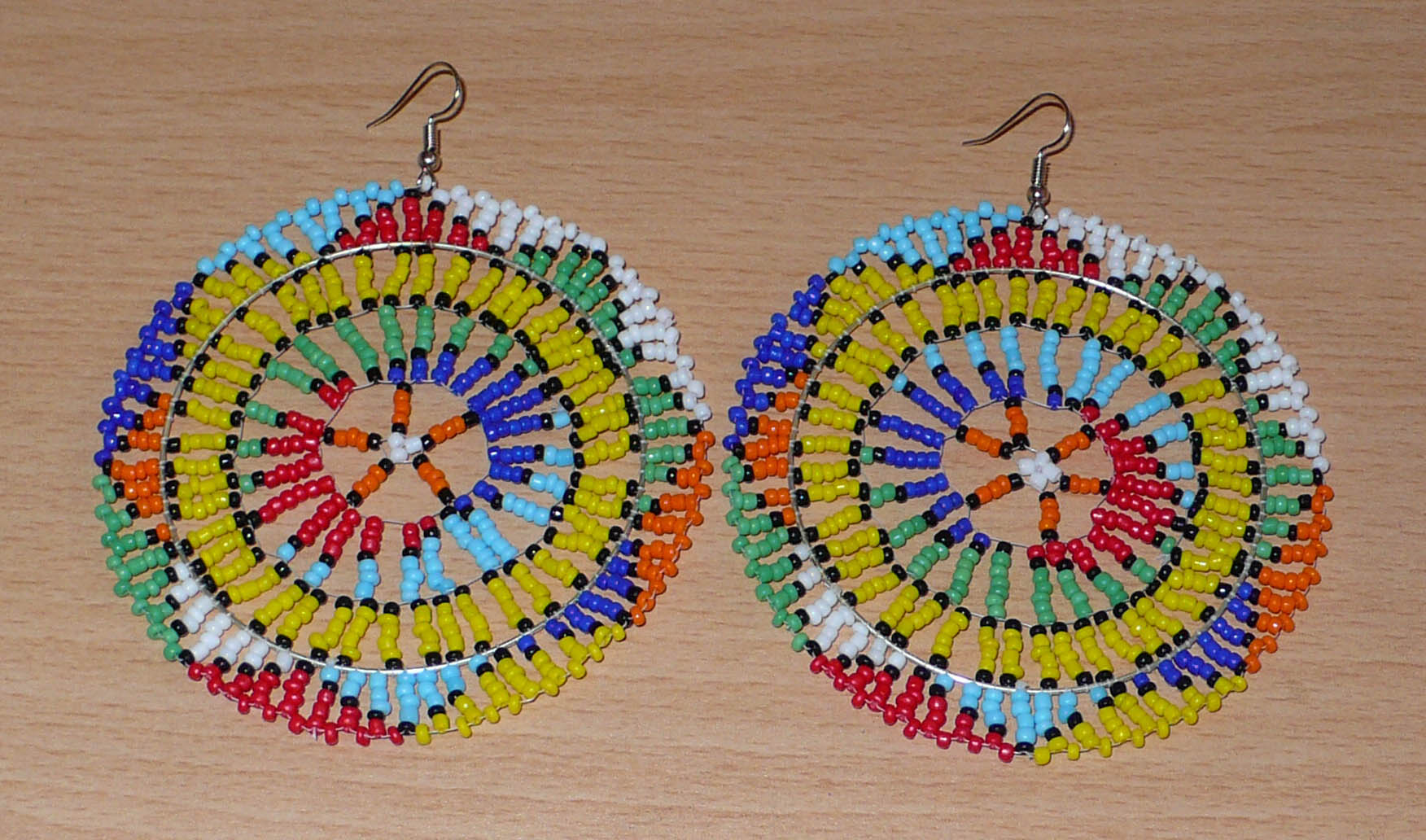 Boucles d'oreilles sud-africaines rondes au style afro chic des années 70. Elles se composent de perles de rocaille multicolores enfilées sur des fils de nylon fixés sur des structures circulaires. Surdimensionnées, elles mesurent 10 cm de long et 8,5 cm de large, et se portent sur des oreilles percées.