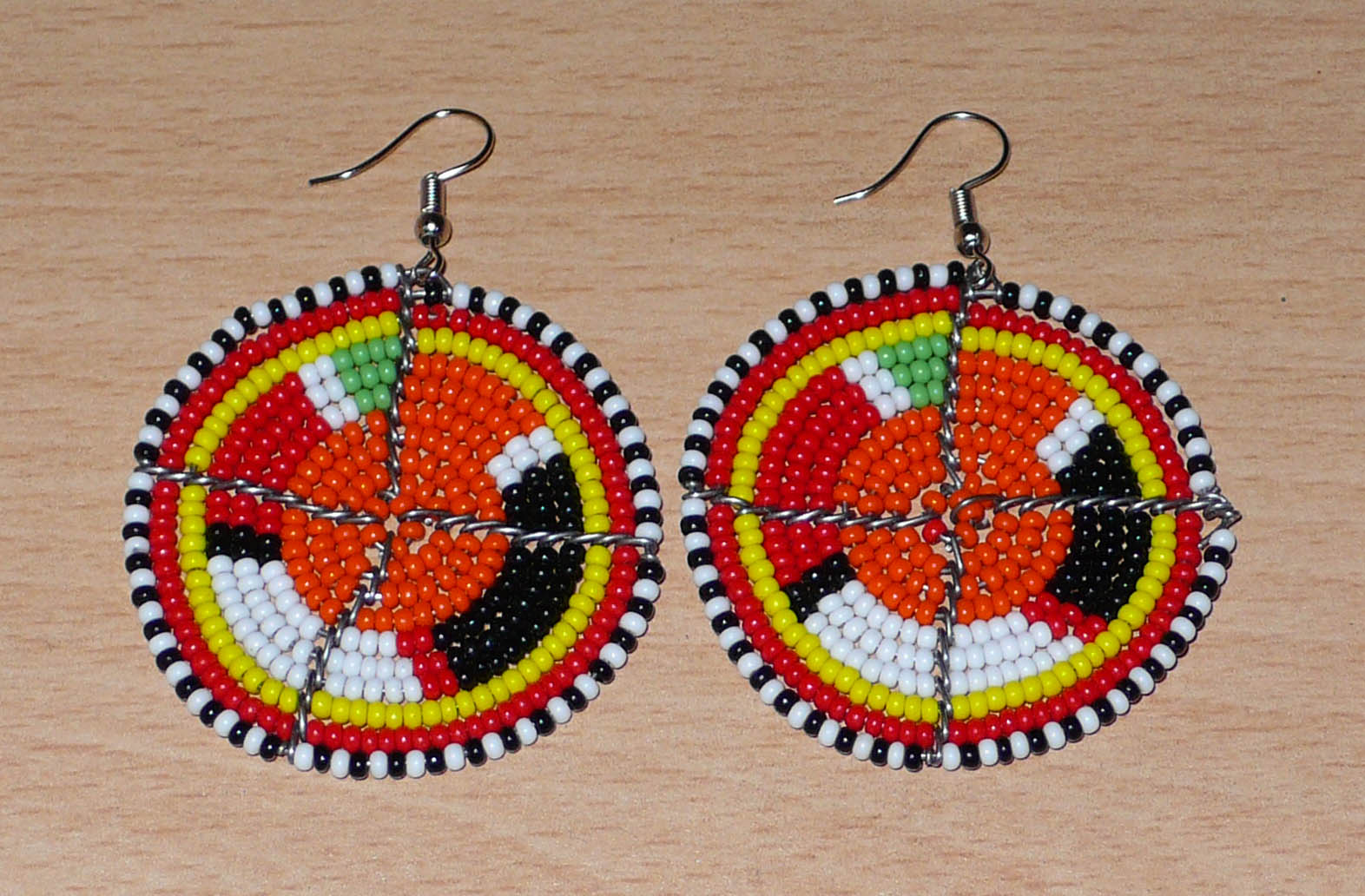 Boucles d'oreilles africaines Massai rondes en perles de rocaille orange et multicolores ; de taille moyenne, elles mesurent 6,5 cm de long et 4,5 cm de large, et se portent avec des crochets en acier inoxydable.