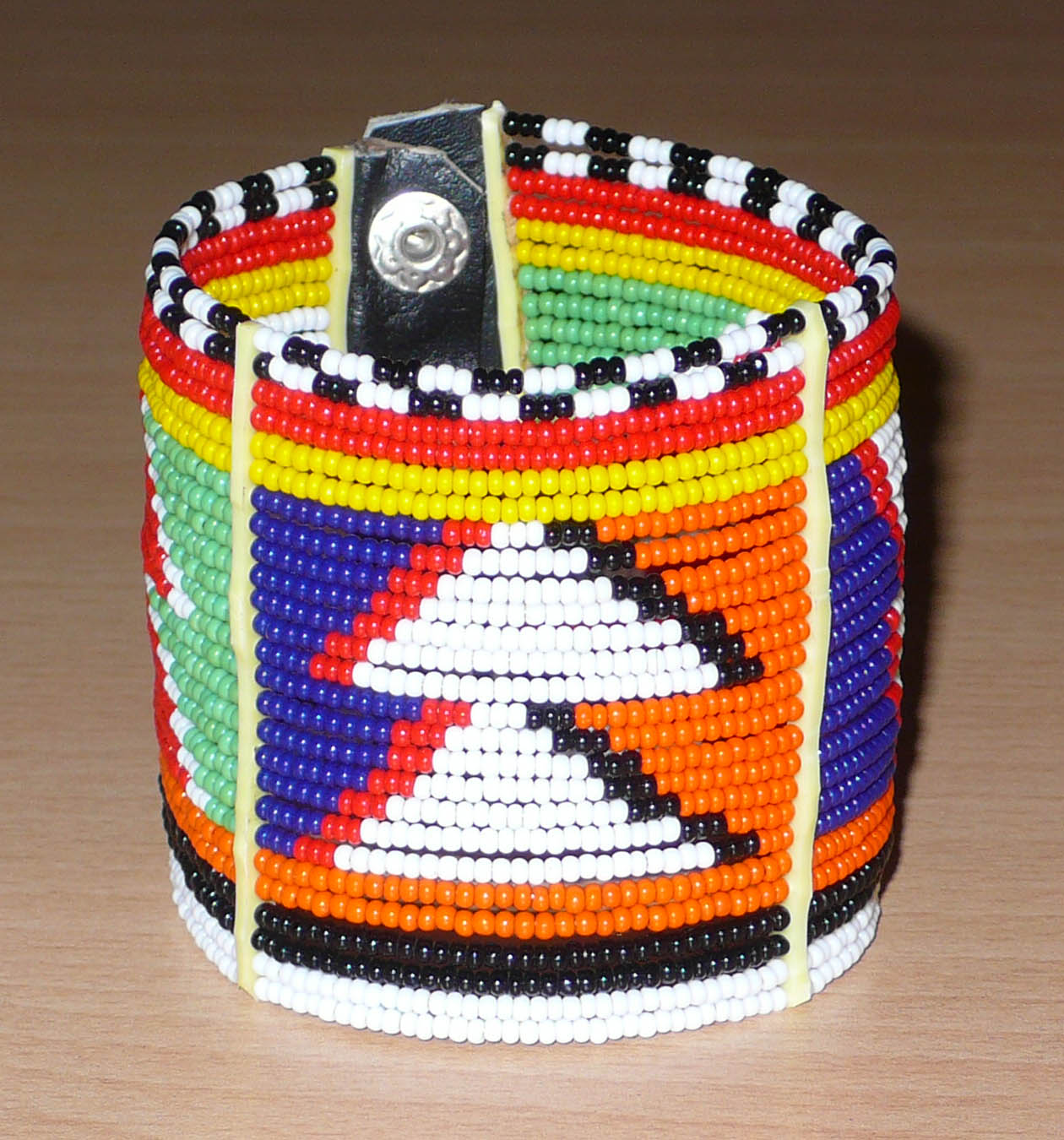Bijou africain. Bracelet africain traditionnel aux motifs et couleurs Massai composé de perles de rocaille multicolores enfilées sur vingt-six rangées de fils de fer fixés sur de charnières en plastique. Fermé, il mesure 19,5 cm et a une hauteur de 6 cm. Il s'attache avec trois boutons pressions. Timeless Fineries
