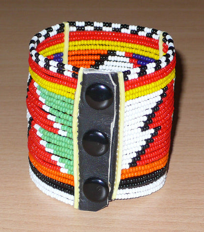 Bijou africain. Bracelet africain traditionnel aux motifs et couleurs Massai composé de perles de rocaille multicolores enfilées sur vingt-six rangées de fils de fer fixés sur de charnières en plastique. Fermé, il mesure 19,5 cm et a une hauteur de 6 cm. Il s'attache avec trois boutons pressions. Timeless Fineries