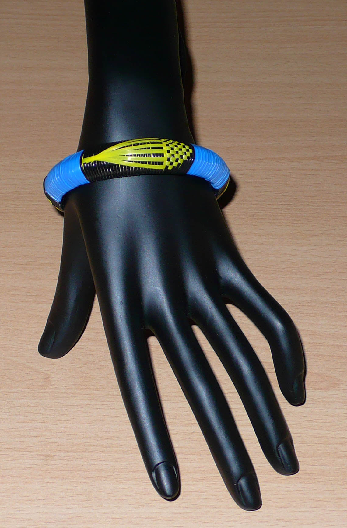 Conçu au Mali dans une démarche eco-responsable, ce bracelet africain à motifs ethniques se compose de fines bandes de plastique recyclé noir, bleu et jaune.  Le bracelet a une circonférence interne de 19,5 cm, un diamètre de 6,5 cm et une épaisseur de 1,3 cm.  Il peut être porté par une femme ou par un homme. Timeless Fineries