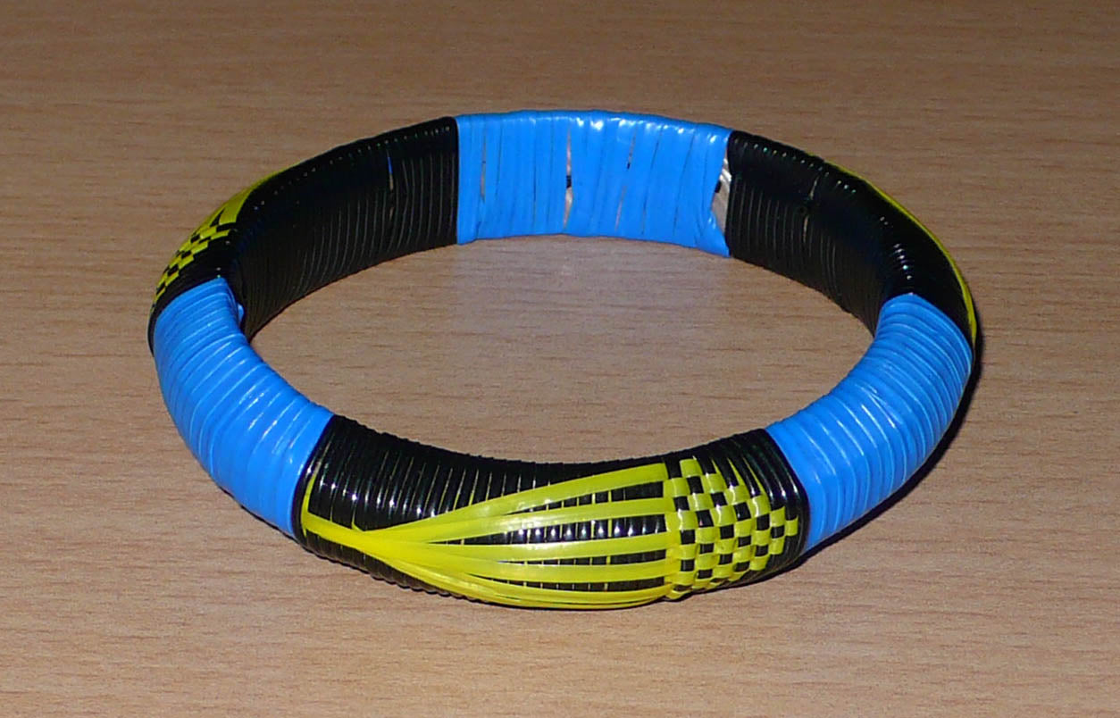 Conçu au Mali dans une démarche eco-responsable, ce bracelet africain à motifs ethniques se compose de fines bandes de plastique recyclé noir, bleu et jaune.  Le bracelet a une circonférence interne de 19,5 cm, un diamètre de 6,5 cm et une épaisseur de 1,3 cm.  Il peut être porté par une femme ou par un homme.