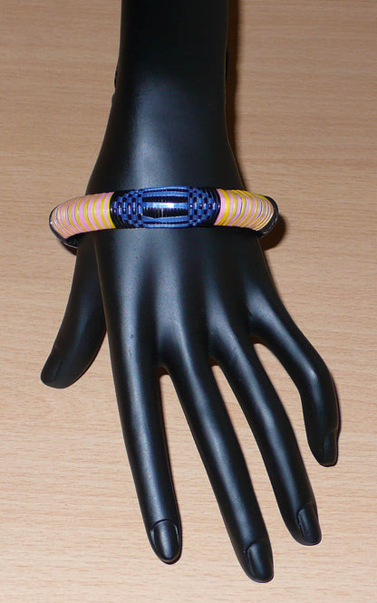 Bracelet africain eco-friendly à motifs tribaux tressés avec de fines bandes de plastique recyclé noir, bleu, rose et jaune.  Ce bracelet a une circonférence interne de 20,5 cm, un diamètre de 6,5 cm et une épaisseur d'1,3 cm. Timeless Fineries