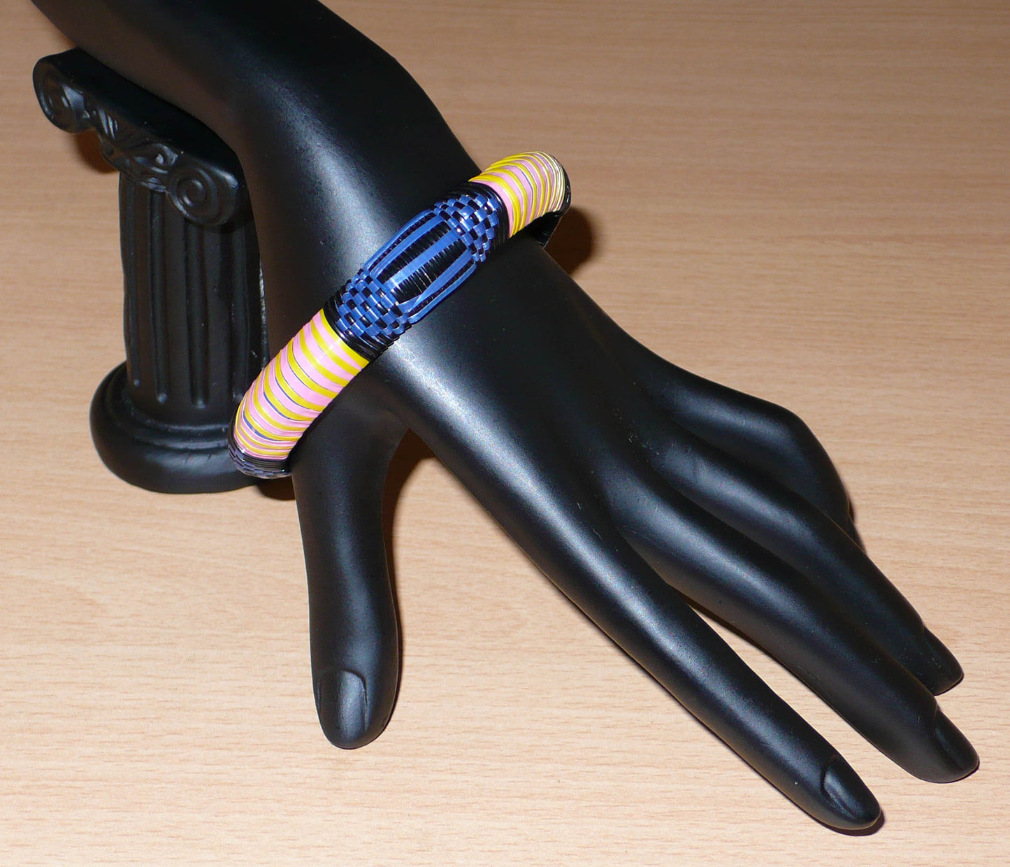 Bracelet africain eco-friendly à motifs tribaux tressés avec de fines bandes de plastique recyclé noir, bleu, rose et jaune.  Ce bracelet a une circonférence interne de 20,5 cm, un diamètre de 6,5 cm et une épaisseur d'1,3 cm. Timeless Fineries
