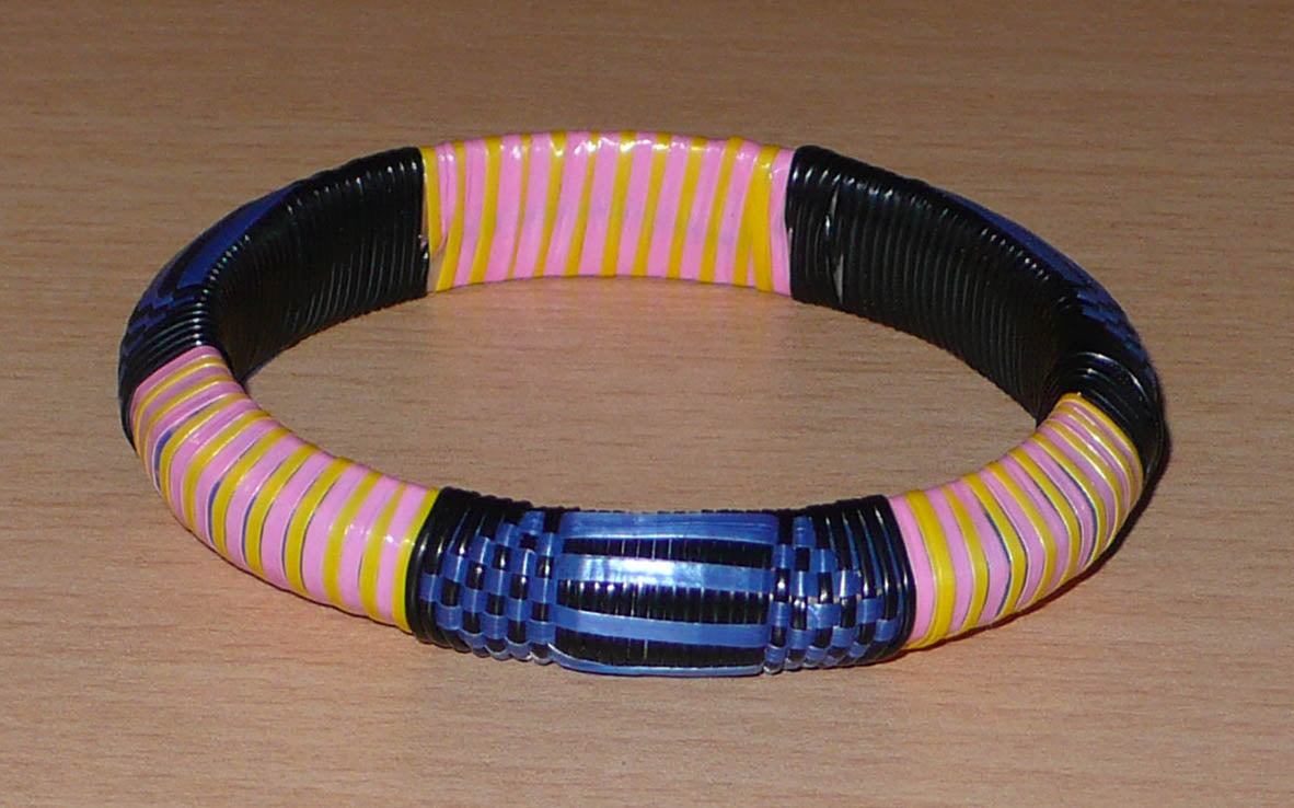 Bracelet africain eco-friendly à motifs tribaux tressés avec de fines bandes de plastique recyclé noir, bleu, rose et jaune.  Ce bracelet a une circonférence interne de 20,5 cm, un diamètre de 6,5 cm et une épaisseur d'1,3 cm.