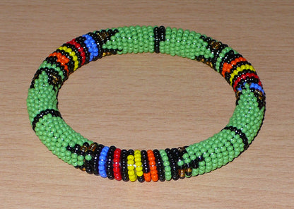 Bracelet africain traditionnel composé de perles de rocaille vertes et de motifs zoulous multicolores. Il mesure 21 cm de circonférence interne, 6,5 cm de diamètre interne et a une épaisseur d'1 cm.