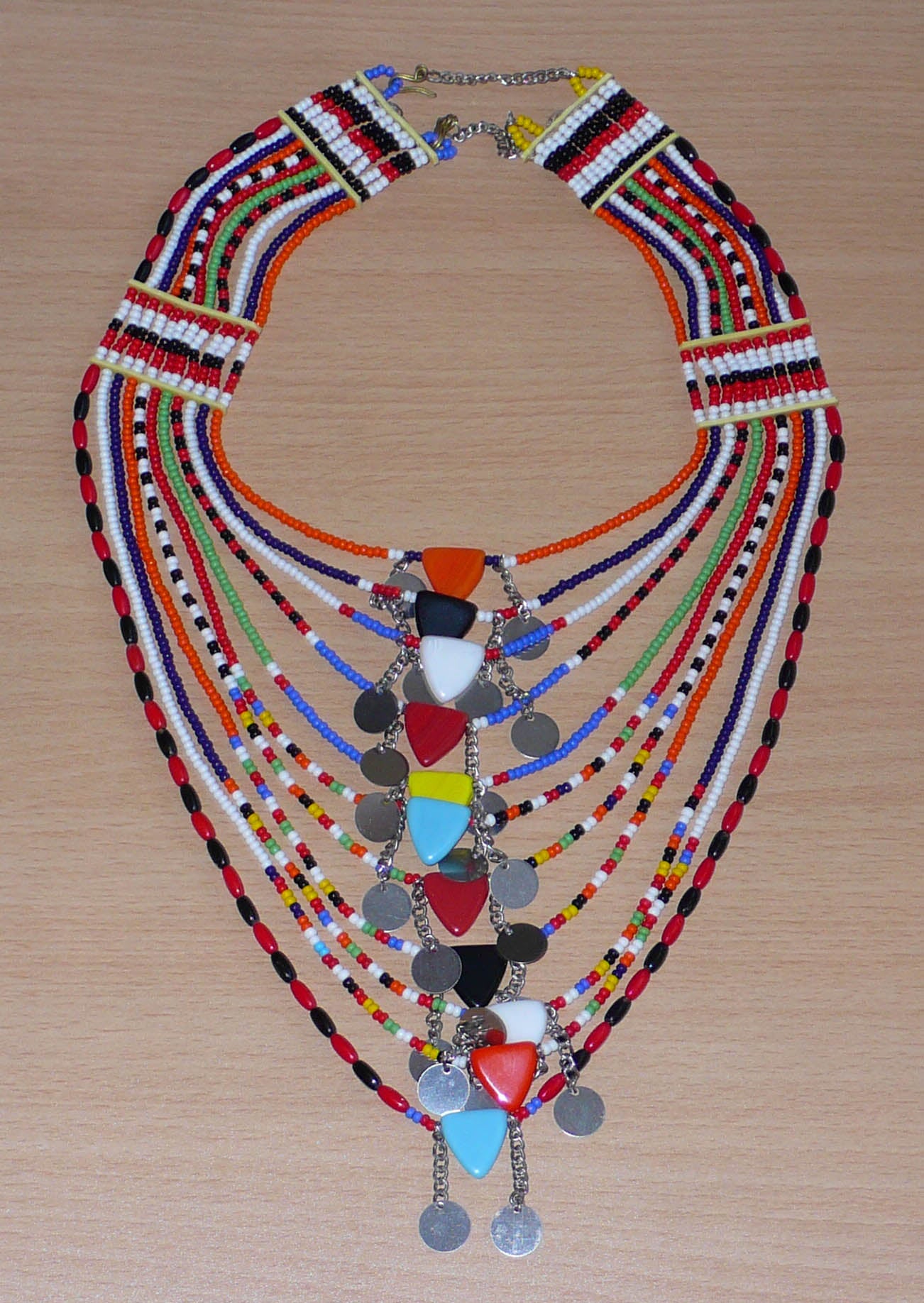 Collier africain traditionnel Massai composé de onze rangées de perles de rocaille et de plastique multicolores. Des perles triangulaires colorées et des pastilles en métal décorent le collier en son centre. Il mesure 38 cm de long, avec une longueur de tour de cou de 46 cm. Timeless Fineries