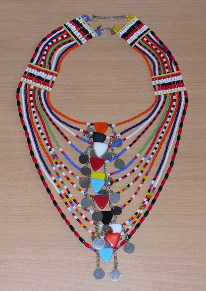 Collier africain traditionnel Massai composé de plusieurs rangées de perles multicolores ; des perles triangulaires et des pastilles en métal décorent le collier en son centre.