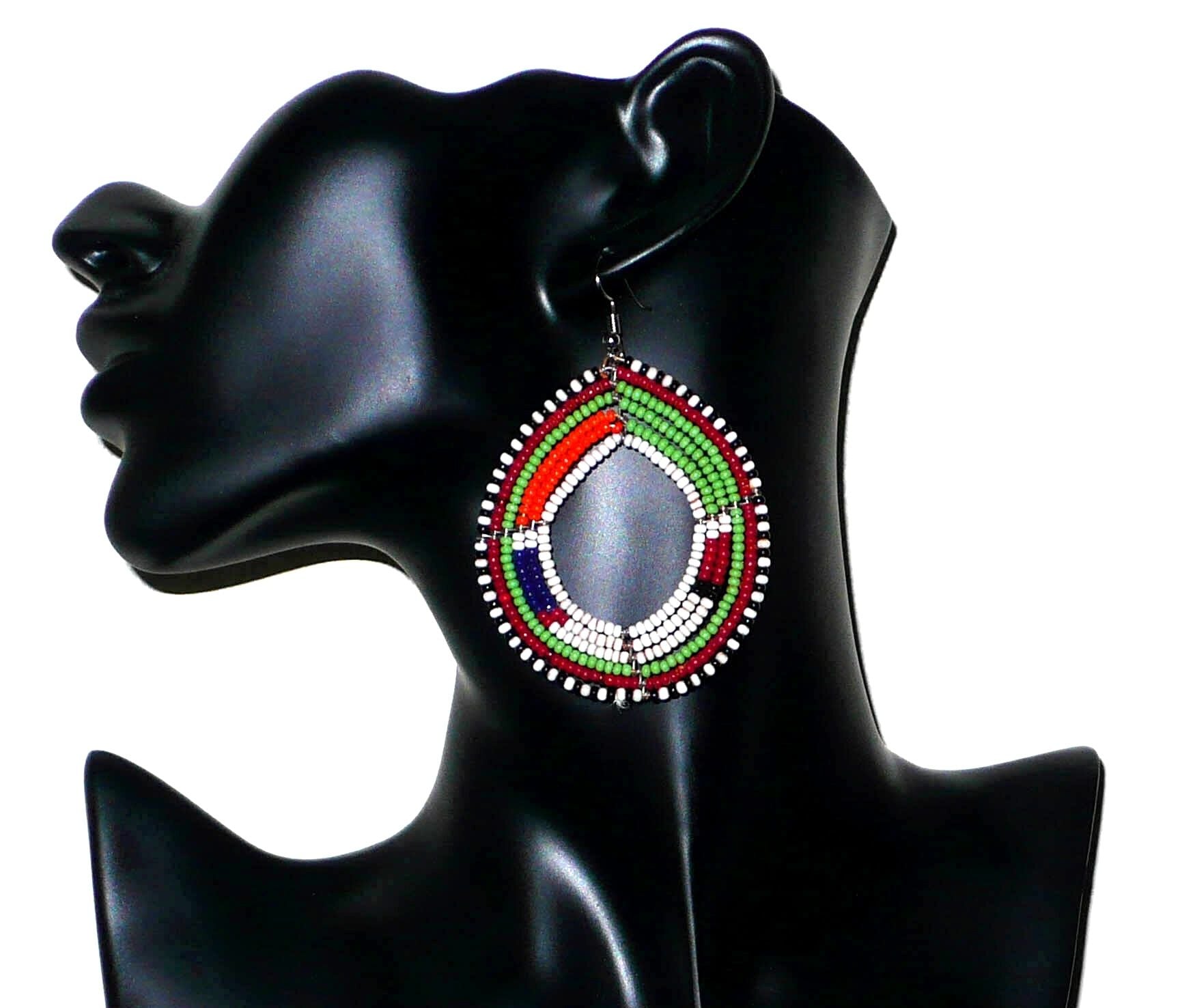 Longues boucles d'oreilles africaines Massai faites de perles de rocaille vertes, blanches, orange, rouges, bleu foncé et noires fixées sur six rangées de fils de fer montés en cercles. Elles mesurent 8 cm de long et 5,5 cm de larges et se portent avec des crochets en acier inoxydable sur des oreilles percées. Timeless Fineries