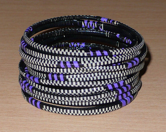 Ensemble de 12 bracelets africains tricolores fabriqués au Mali dans une approche éco-responsable ; très fins, ils se composent de fines bandes de plastique recyclé violet, noir et blanc.  Ces bracelets ont une circonférence de 19,5 cm, un diamètre de 6,3 cm et une épaisseur de 0,4 cm.  Ils peuvent être portés par une femme ou par un homme. Timeless Fineries