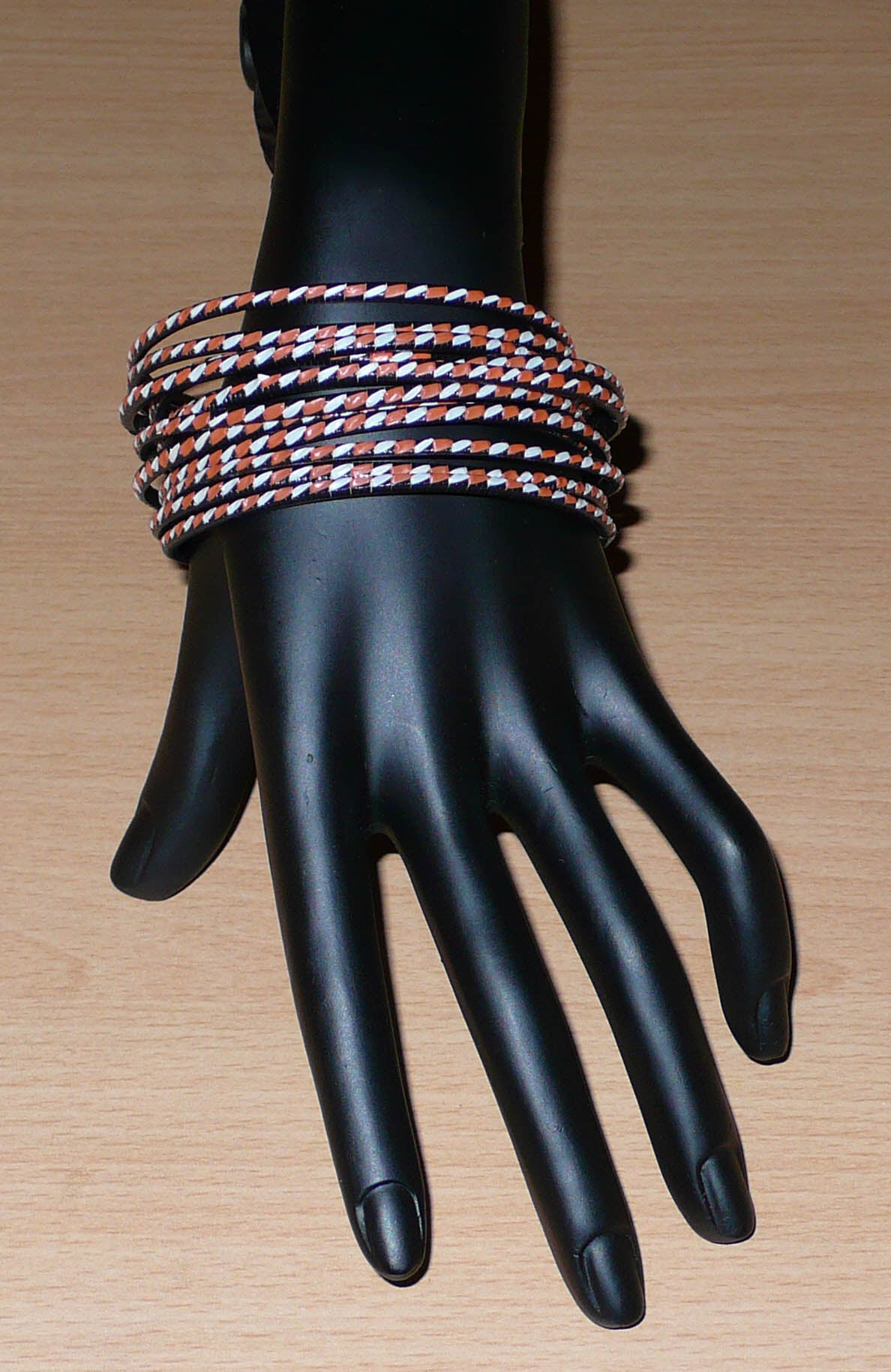 Ensemble de 12 bracelets africains tricolores tressés à partir de plastique recyclé orange, blanc et noir.  Très fins, ces bracelets ont une circonférence de 21 cm, un diamètre de 6,8 cm et une épaisseur de 0,3 cm.