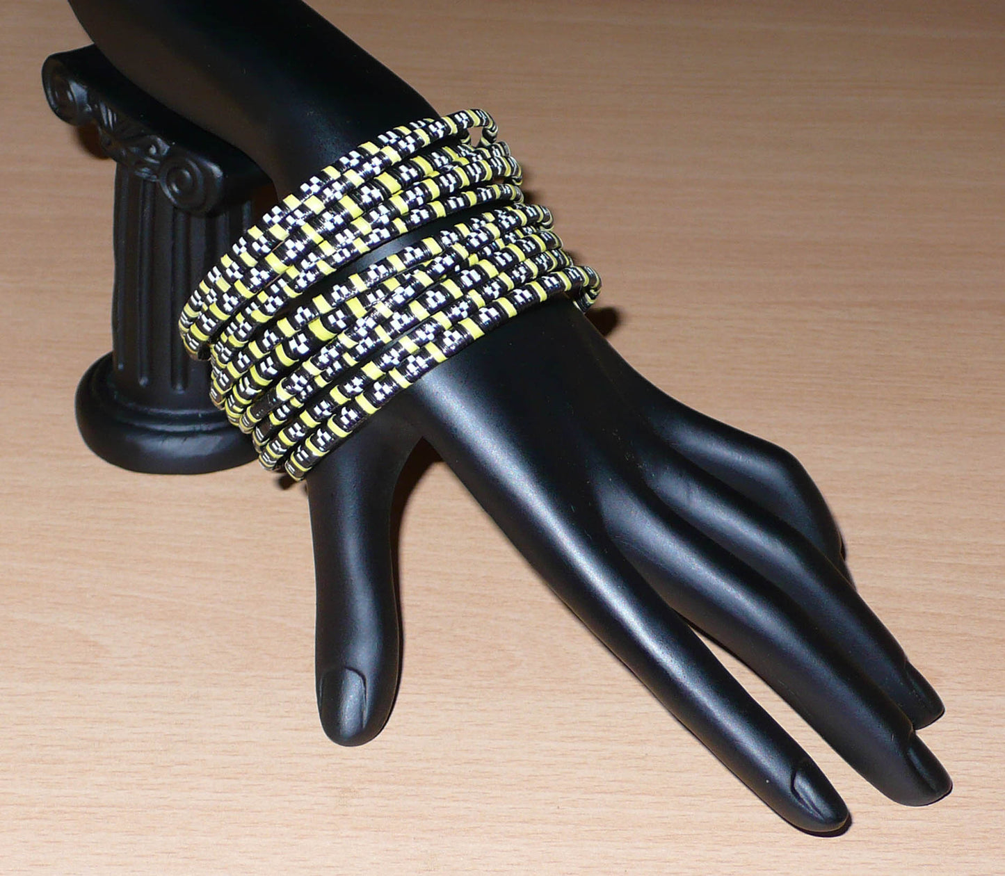 Empilez-les sur vos poignets ! Ensemble de 12 bracelets africains tricolores fabriqués au Mali à partir de fines bandes de plastique recyclé noir, jaune et blanc.  Ces bracelets, très fins, ont une circonférence de 20,5 cm, un diamètre de 6,5 cm et une épaisseur de 0,5 cm.  Ils peuvent être portés par une femme ou par un homme.